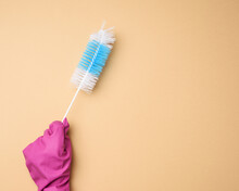 Hand In A Rubber Glove Holds A Brush For Washing Bottles On A Beige Background