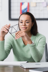 Canvas Print - young african american architect holding model of pyramid near laptop on blurred foreground