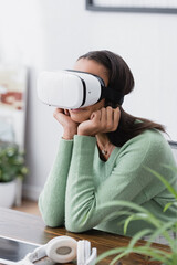 Canvas Print - african american designer sitting in vr headset at workplace near headphones, blurred foreground