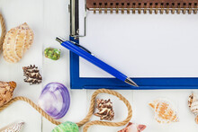Summer Vacation Concept. Sea Shells With Rope On White Wooden Background, Notebook With Pen For Summer Plan, Copy Space