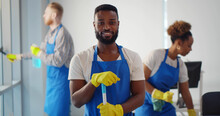 Portrait Of African Cleaner In Apron And Gloves Holding Mop And Smiling At Camera Working In Office