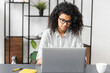 © Vadim Pastuh - Concentrated young African American office worker businesswoman with Afro hairstyle in glasses sitting at the desk in the home office, working on a laptop. A student stressing, taking an online exam