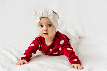stylish infant in trendy white headband on bed. .cute baby girl in red sweater with hearts lying and