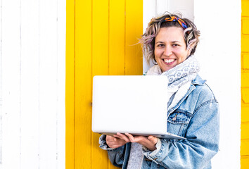 Poster - Caucasian female with a face mask making a video call on a laptop against a white and yellow wall