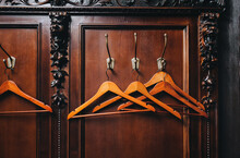 Wooden Hangers Hang In An Empty Closet On The Hooks Of A Wardrobe Rack Made Of Carved Natural Mahogany (redwood). The Concept Of The Absence Of Guests Or Visitors To A Theater Or Restaurant.