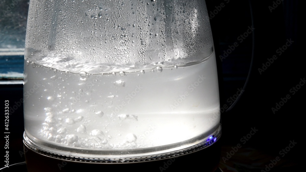 Defocused bubbles in hot water boiling inside glass teapot in bright ...