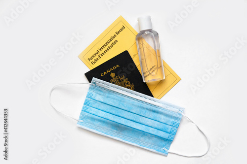 Canadian passport with yellow immunity vaccination record in English and French languages, face mask and sanitizer. Safety measures against coronavirus covid-19 spread around world.