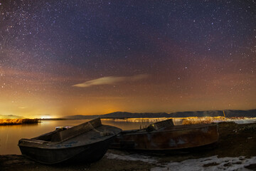 Winter landscape, beautiful frozen lake and two boats on the beach in night under the starry sky.