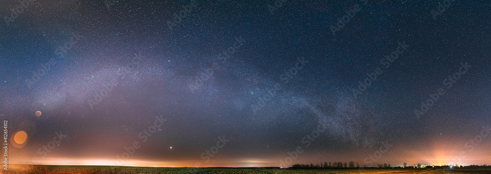 Night Starry Sky With Glowing Stars Above Countryside Landscape. Milky Way Galaxy And Rural Field Meadow In Early Spring. Panorama, Panoramic View - obrazy, fototapety, plakaty 