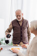© LIGHTFIELD STUDIOS - senior man in glasses pouring red wine in glass of retired woman