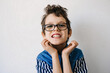 Portrait of autistic boy with glasses in blue shirt on a white backdrop smiling and grimaces. Autism awareness concept
