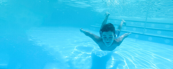 Boy swimming under blue water in pool