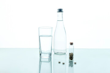 Wall Mural - Pills in a transparent jar with a glass of water and a glass bottle on a white background. Medical concept.