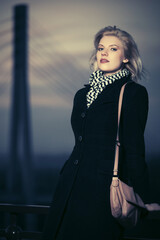 Wall Mural - Fashion blond woman in black coat leaning on railing