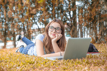 Wall Mural - Caucasian teenager girl lying down on the grass using laptop