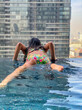 © jovannig - Young girl enjoying city view from a high viewpoint in the pool, back view. Modern cityscape and vacation concept