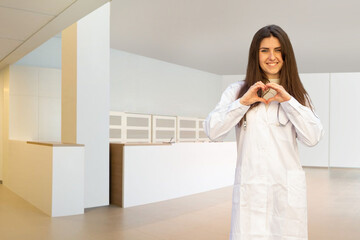 Lovely young Caucasian female doctor or nurse showing heart shape with hands