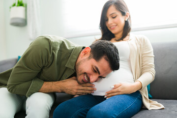 Wall Mural - Excited latin man hearing his baby moving in the belly of his wife