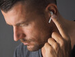 © Andrei - Man wearing wireless earphone and touching one earphone to control application. Close-up Headshot.