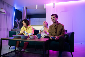 Young friends play video games while sitting on a couch in a living room.