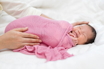 happy newborn baby wrap in blanket and parent hands on bed