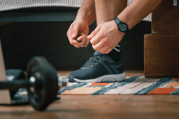 Wall Mural - Close-up of a man tying shoelaces in black sports sneakers, a sports black watch on his hand, and metal dumbbells nearby