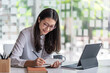© amnaj - Asian businesswoman meeting at the office, taking notes and using a tablet at the office.