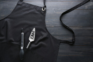 Clean apron and kitchen utensils on dark background