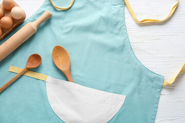 Wall Mural - Clean apron, kitchen utensils and eggs on light background, closeup