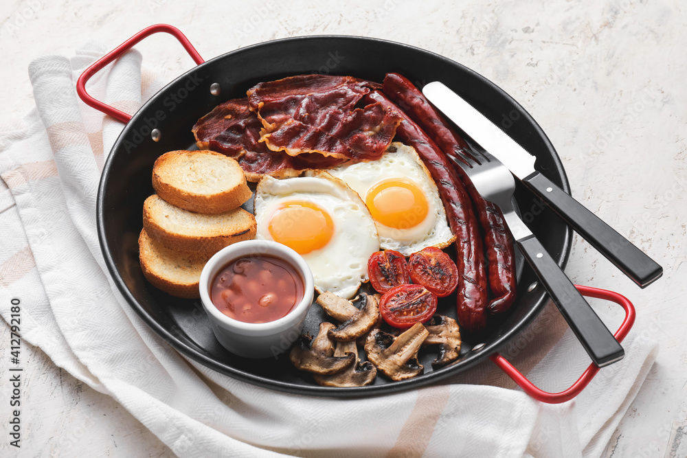 Traditional English breakfast with fried eggs in pan on light background