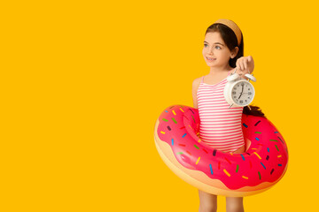 Wall Mural - Cute little girl in swimsuit, with alarm clock and inflatable ring on color background