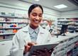 © StratfordProductions - Portrait of cheerful young woman browsing digital tablet working in pharmacy with colleague in background