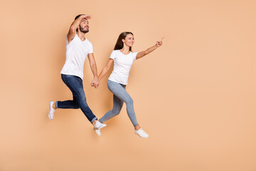 Poster - Full length photo of young couple happy smile jump go girl point finger empty space guy look ahead isolated over beige color background