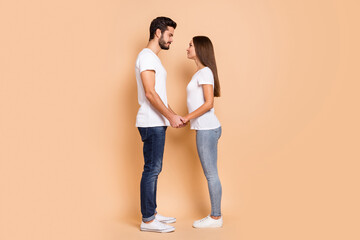 Wall Mural - Full length photo of pretty husband wife wear white t-shirts smiling holding hands arms isolated beige color background