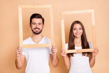 Sticker - Photo of charming married couple dressed white t-shirts holding photo frames smiling isolated beige color background