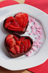 Two mini heart shaped chocolate tarts with fresh strawberries on a plate on a wooden table