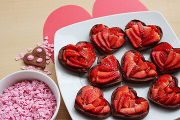 Wall Mural - Valentine’s day dessert background. Mini heart shaped chocolate tarts with fresh strawberries and glazed ccokies with sprinkles on a wooden table