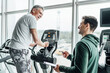 Portrait of an older man during training, his physiotherapist is standing next to him and tells how to do the exercise correctly