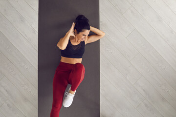 Top view of sporty active woman doing cross training bicycle crunches trains leg muscles and abs. Athlete conducts daily training on a mat in the room. Banner. Place for text. Article for website.