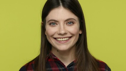 Wall Mural - Close up portrait cheerful beautiful woman in checkered shirt looking at camera with toothy smile, healthy and positive, enjoying life. Indoor studio shot isolated on yellow background