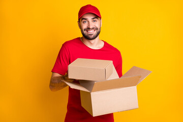 Wall Mural - Photo of cheerful guy courier dressed red clothes holding delivering brown boxes isolated yellow color background