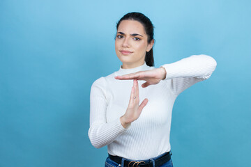 Wall Mural - Young caucasian woman wearing white sweater over blue background Doing time out gesture with hands, frustrated and serious face