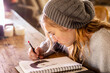 © Mint Images - Teenage girl in a woolly hat drawing with a pencil on a sketchpad.