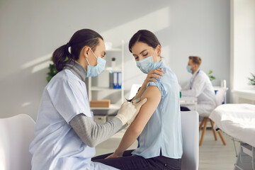 Vaccination campaign during global Covid 19 pandemic. Young woman gets vaccinated at clinic or health center. Nurse or doctor in medical face mask gives antivirus vaccine shoulder injection to patient