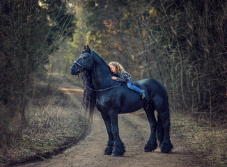 Beautiful girl sitting on black Frisian horse  in spring in the forest