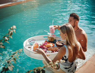 Tattooed woman with her handsome boyfriend enjoys tropical food and swim in a pool in Thailand.