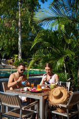 Romantic portrait of a two travellers which eat exotic food together in hotel with swimming pool in Thailand.