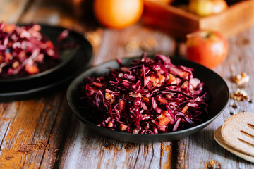 Red cabbage salad (coleslaw) with apples, oranges and walnuts on a dark wooden background, food still life