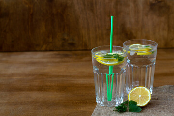 cocktail with lime.summer drinks. glass of lemonade with lemon and fresh leafs mint. homemade cold refreshing drink or water with ice with sackcloth on rustic wood background. Copy space.