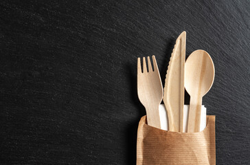 Disposable biodegradable tableware made of wood spoon, knife and fork on marble texture. Close-up.